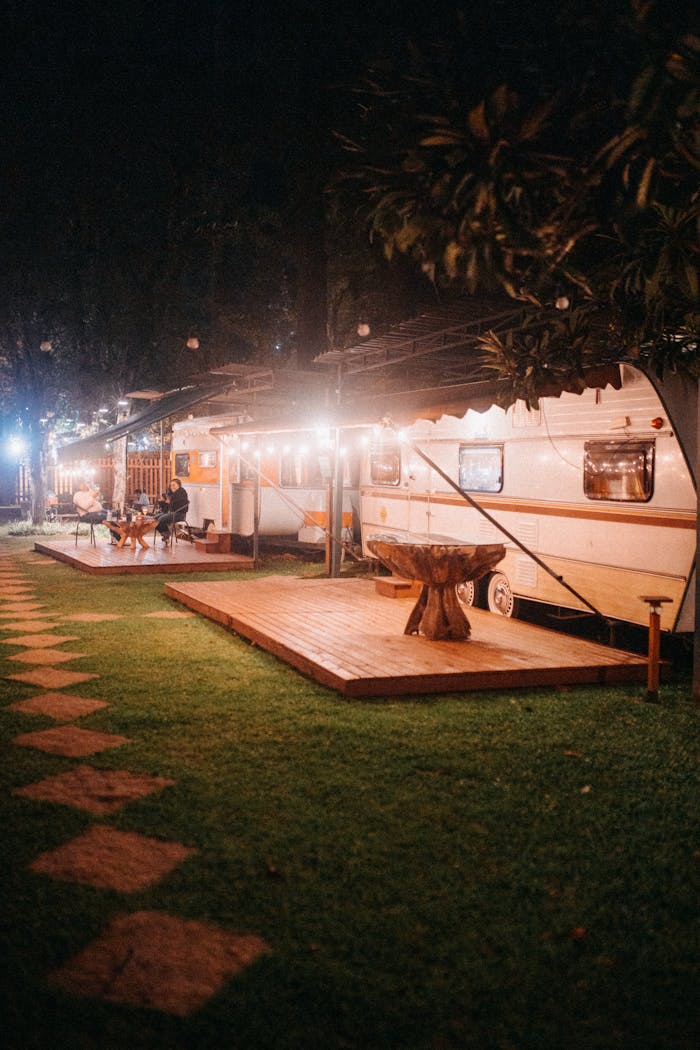 White camping trailers placed in row with small wooden terrace and tables in glowing garlands late at night